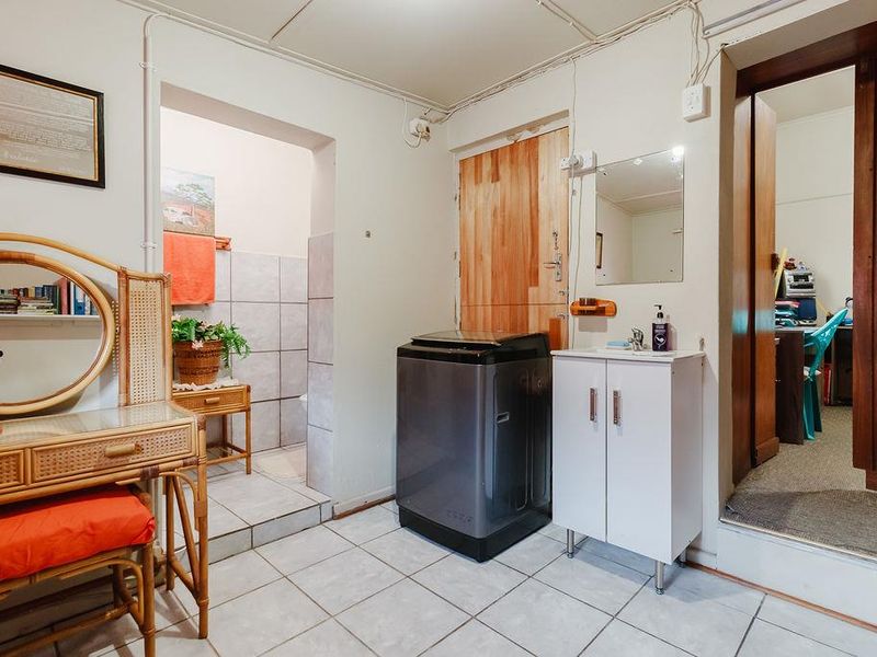 A functional laundry area featuring tiled flooring, a vanity basin, and direct access to an adjacent bathroom and office space.