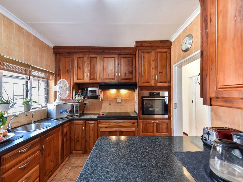 A functional kitchen featuring solid wood cabinetry, granite countertops, built-in oven, extractor fan, and tiled finishes throughout.
