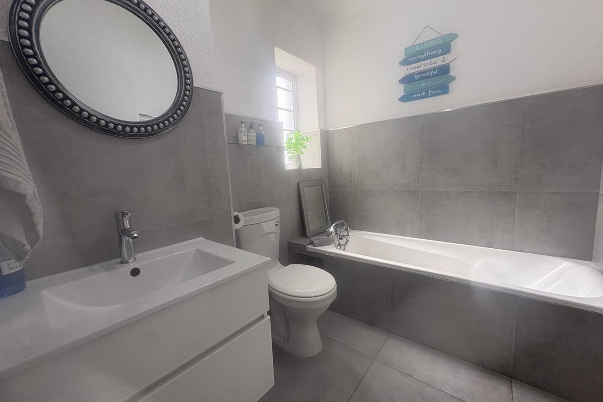 Modern bathroom featuring large format grey wall and floor tiles, a white vanity with basin, a toilet, and a built-in bathtub.