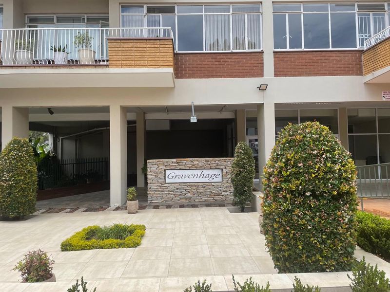 Front entrance area of the Gravenhage apartment complex featuring a stone-clad signage wall, tiled courtyard, and brick facade with balcony access.
