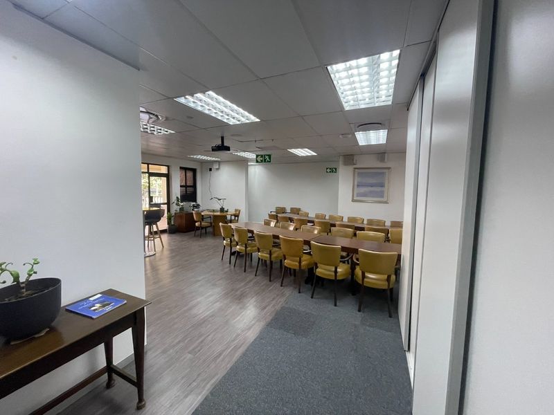 A spacious office area featuring a mix of vinyl and carpet flooring, suspended ceilings with recessed lighting, and a ceiling-mounted projector.
