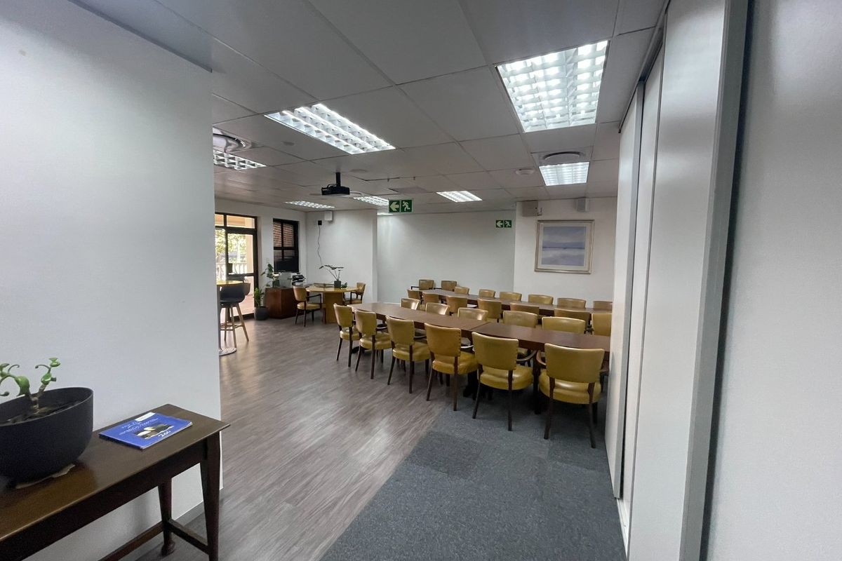 A spacious office area featuring a mix of vinyl and carpet flooring, suspended ceilings with recessed lighting, and a ceiling-mounted projector.