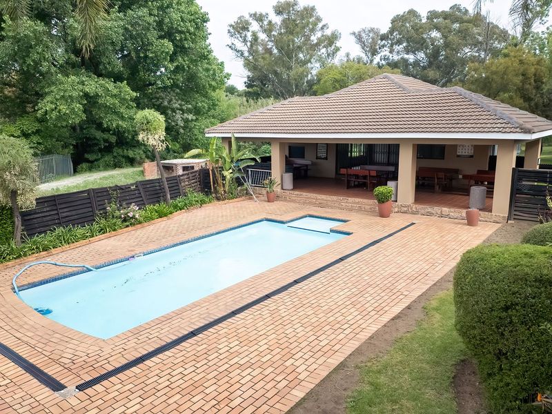Outdoor pool area featuring a swimming pool, brick-paved surround, and a spacious covered patio with a built-in braai, ideal for outdoor entertaining.