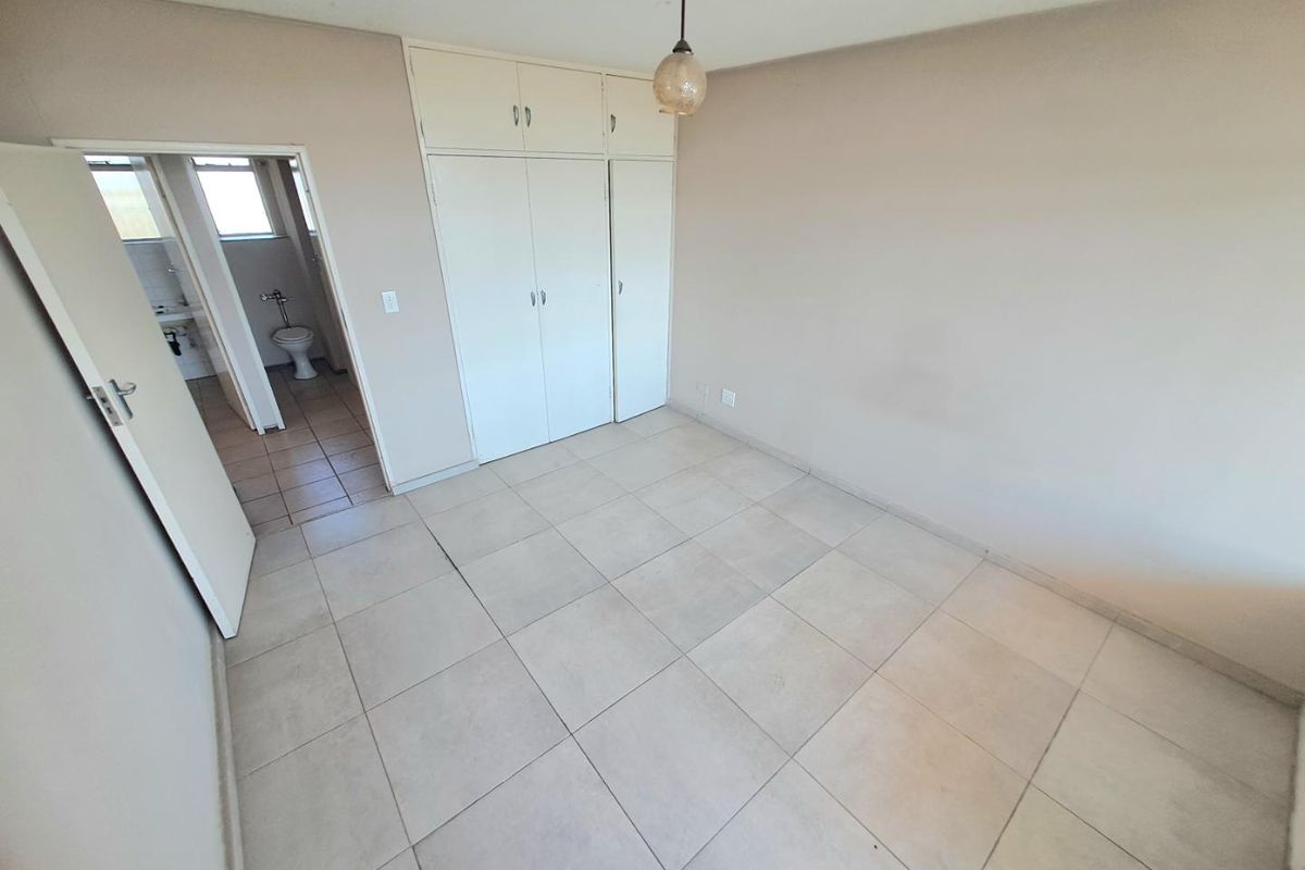 An empty bedroom featuring neutral tiled flooring, built-in cupboards, and an adjacent bathroom entrance.