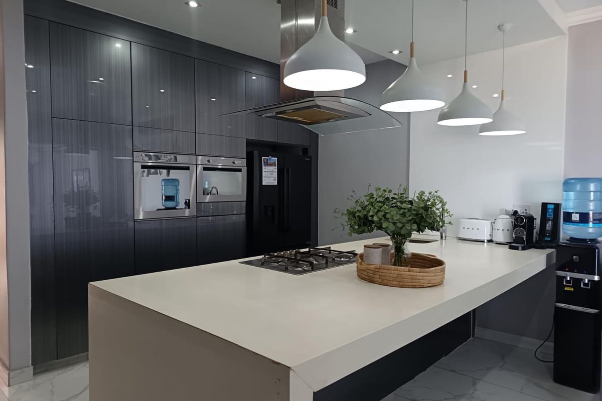 Modern kitchen featuring high-gloss cabinetry, a large central island with a gas cooktop, stone countertops, and integrated appliances under stylish pendant lighting.