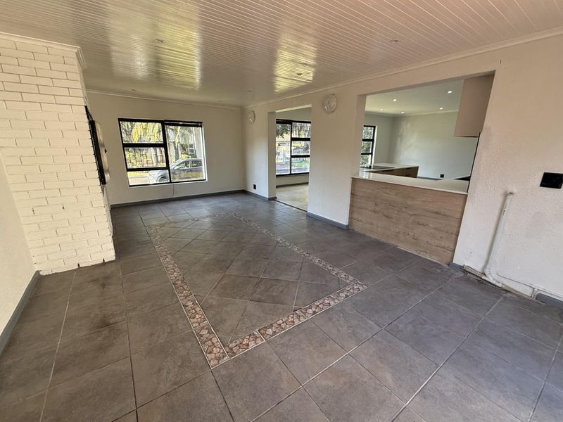 Spacious open-plan living area featuring a brick fireplace, tiled flooring with decorative inlay, and a functional kitchen pass-through with modern cabinetry.