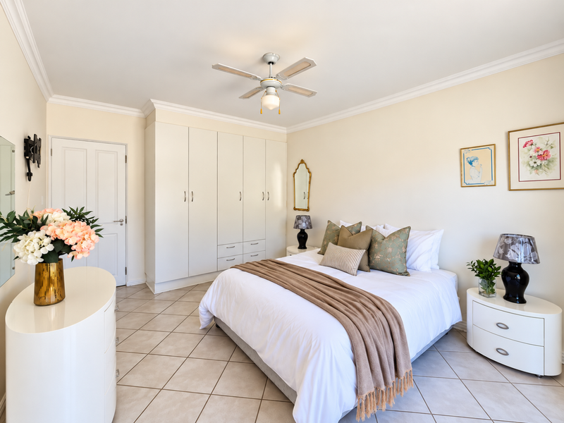A well-maintained bedroom featuring neutral tiled flooring, built-in cabinetry, and a ceiling fan, offering a clean and comfortable living space.