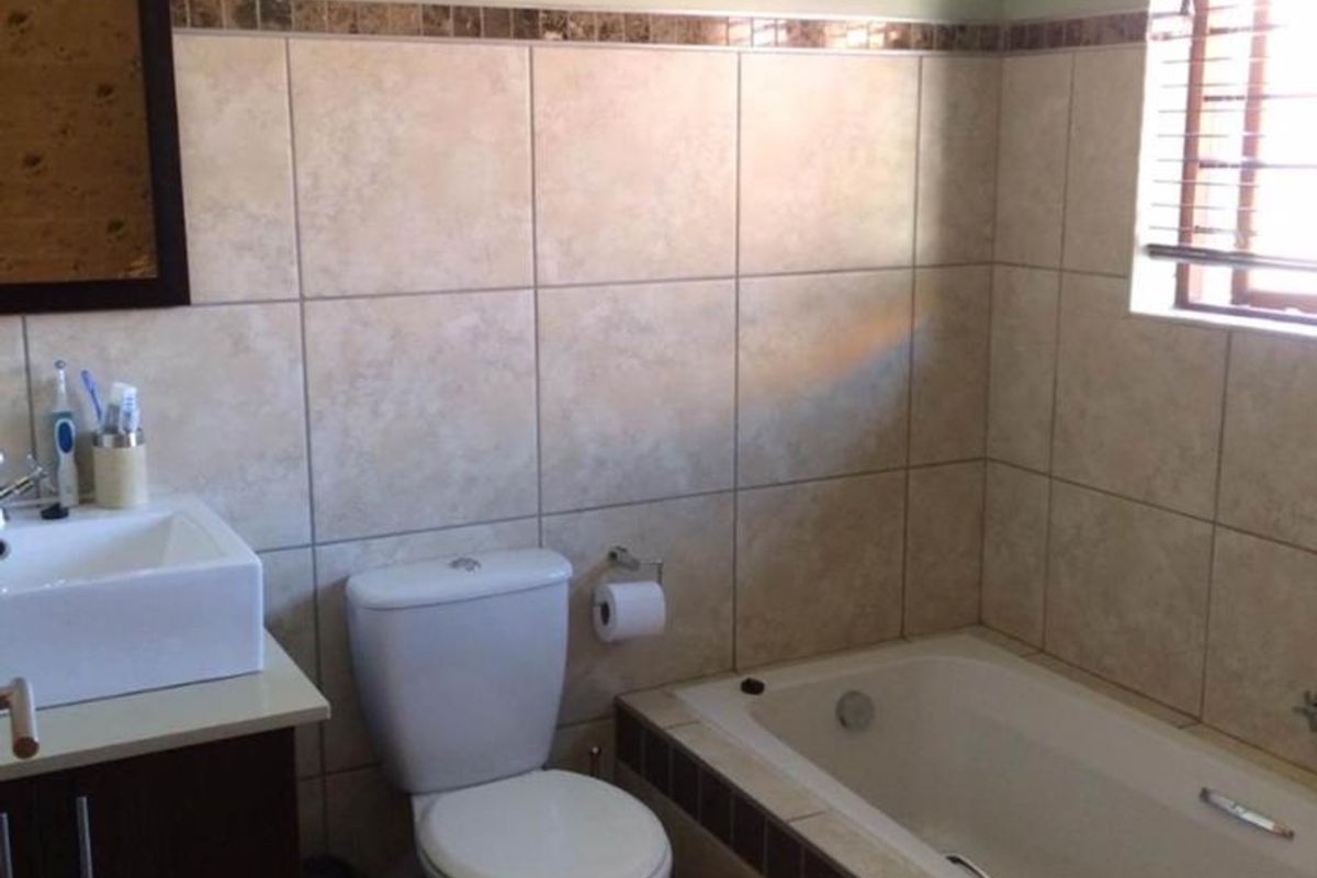 A functional bathroom featuring a built-in vanity with a basin, a standard toilet, and a tiled bathtub surround with neutral wall tiling.