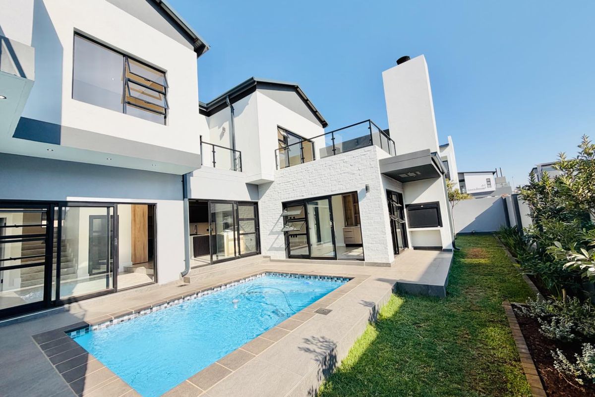 Modern rear elevation featuring a swimming pool, tiled patio area with built-in braai, and contemporary architectural finishes with glass balustrades.
