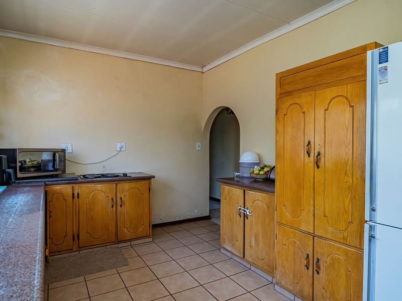 A dated kitchen featuring wooden cabinetry, laminate countertops, and tiled flooring, offering potential for a modern renovation.