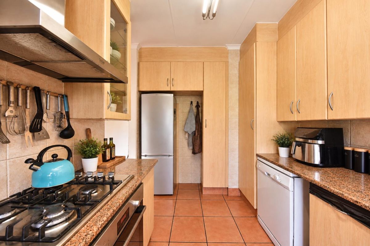 A functional kitchen featuring light wood cabinetry, granite countertops, a gas hob with extractor, and tiled flooring throughout.