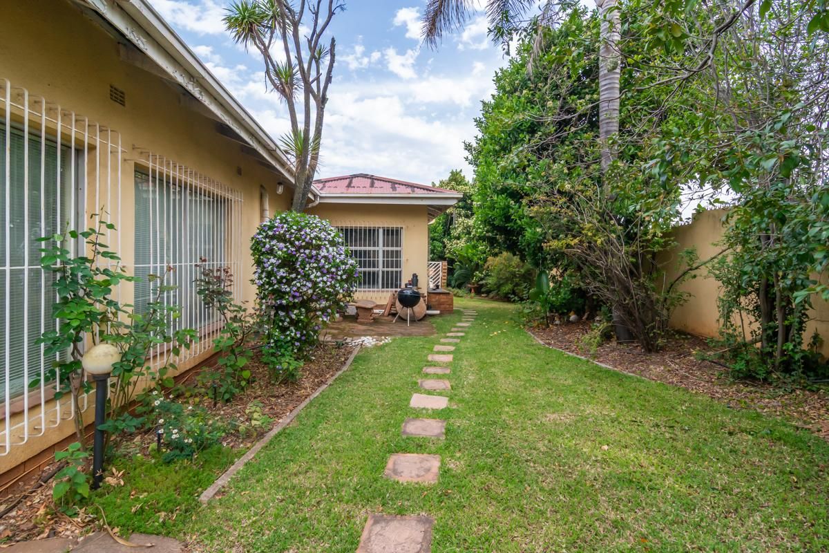 A view of the rear garden featuring a lawn, paved stepping stone path, and established perimeter landscaping alongside the house exterior.