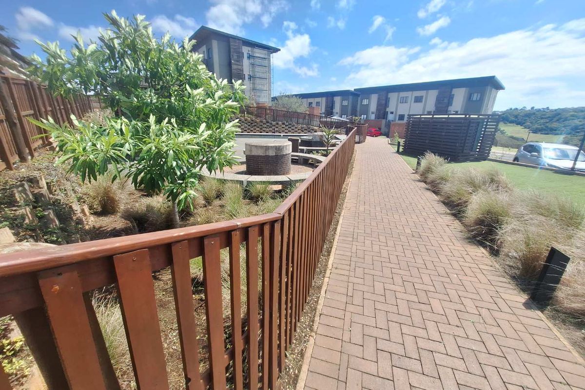 A well-maintained outdoor communal area featuring a paved walkway, timber fencing, and a built-in circular seating area within a landscaped garden setting.