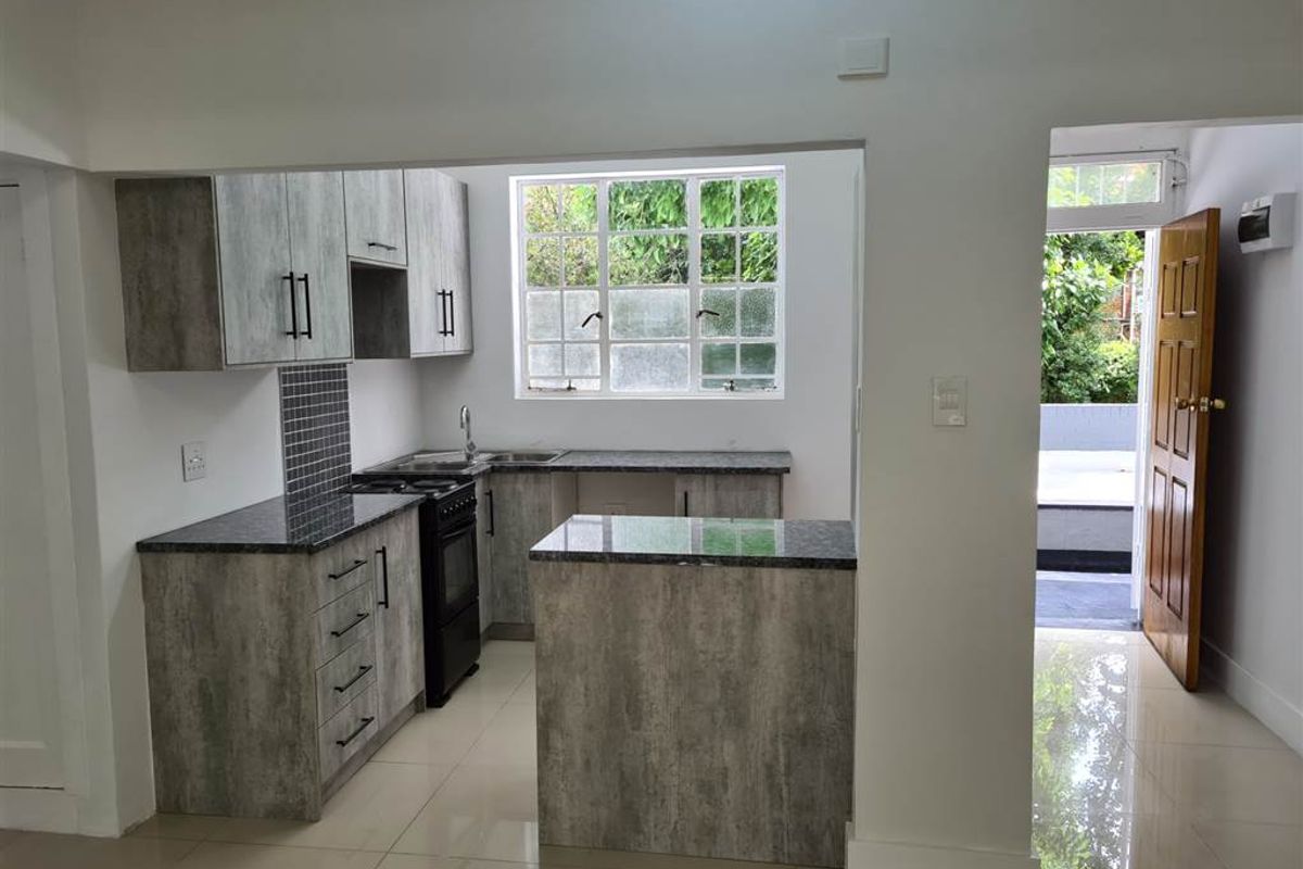 Modern kitchen featuring grey textured cabinetry, granite countertops, tiled backsplash, and a freestanding stove, with direct access to an outdoor area.