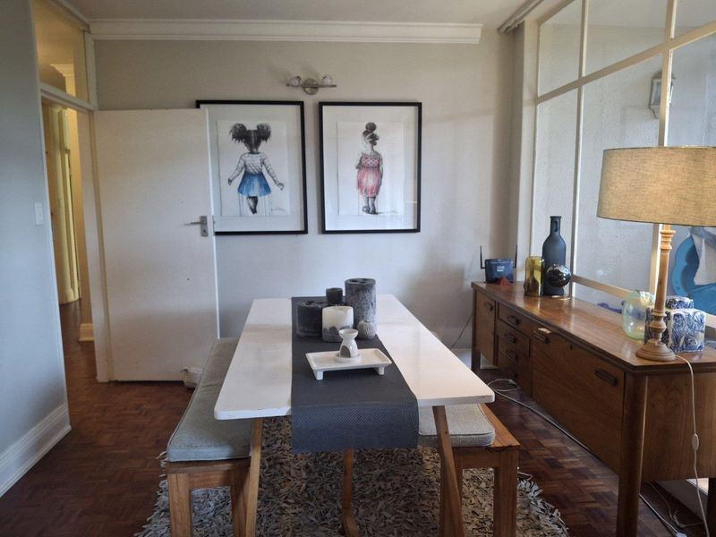 A well-maintained dining room featuring classic parquet flooring, crown molding, and a large internal glass partition that allows for natural light flow.