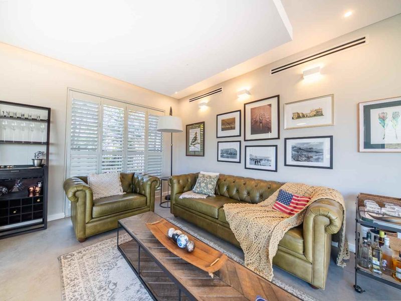 A well-appointed living room featuring polished concrete floors, plantation shutters, and integrated ducted air conditioning with modern wall-mounted lighting.