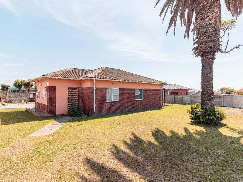 Rear view of a single-story brick and plaster house featuring a tiled roof, security gate, and a spacious garden area.