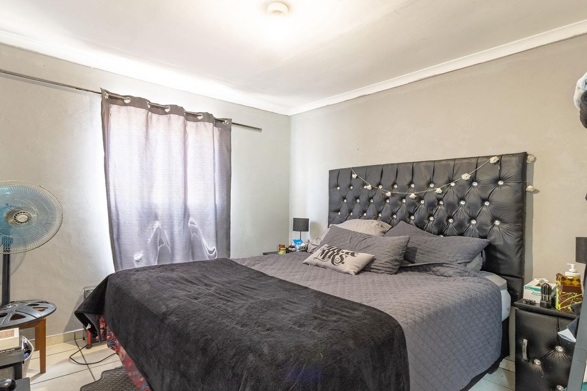 A bedroom featuring tiled flooring, neutral wall tones, and a window with curtain rod installation.