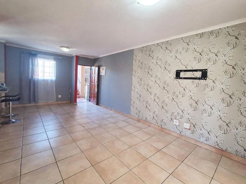 An open-plan living area featuring ceramic floor tiles, a decorative wallpaper feature wall, and a wall-mounted television bracket.