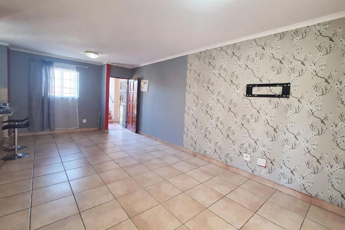 An open-plan living area featuring ceramic floor tiles, a decorative wallpaper feature wall, and a wall-mounted television bracket.