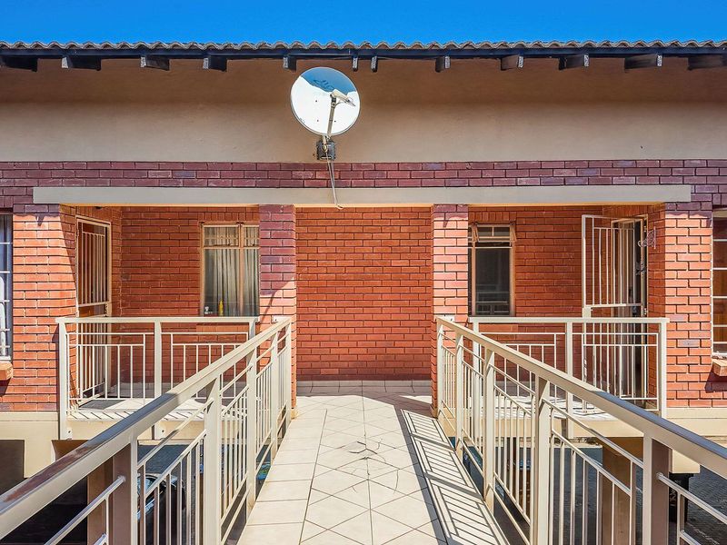 Exterior view of an apartment building featuring a tiled walkway, brick facade, and secure metal railings.