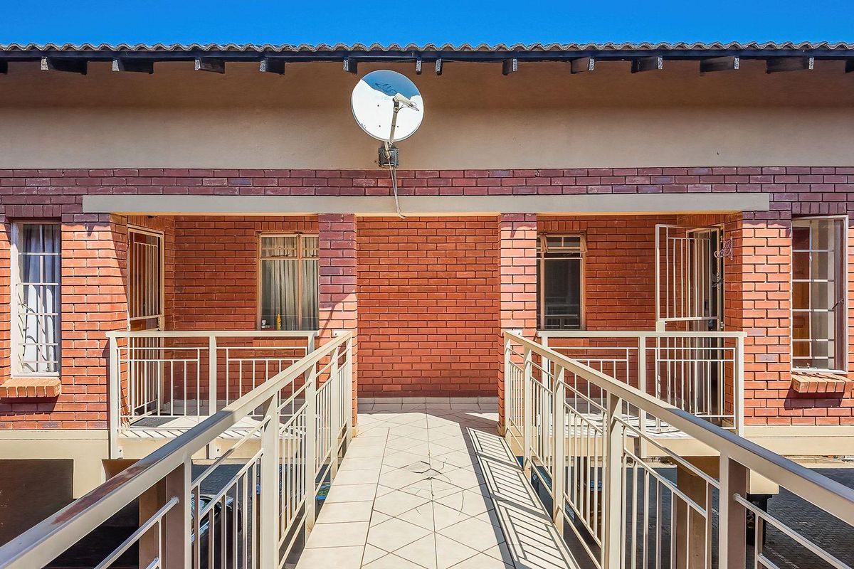 Exterior view of an apartment building featuring a tiled walkway, brick facade, and secure metal railings.