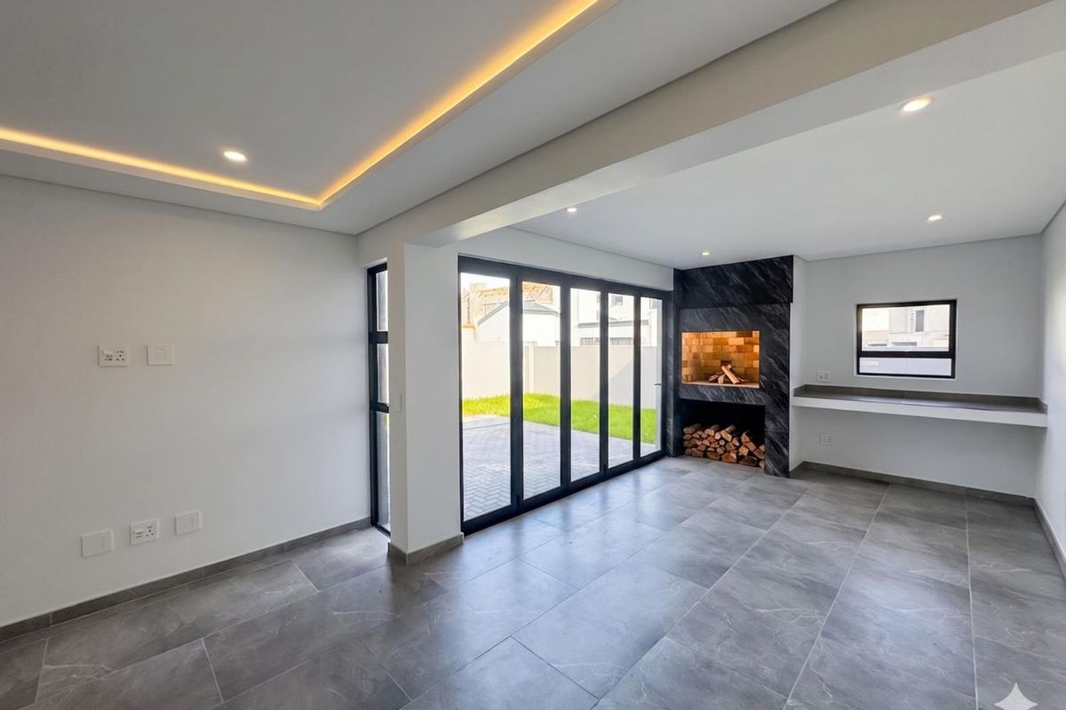 Modern open-plan living area featuring large format floor tiles, recessed ceiling lighting, a built-in fireplace with stone surround, and bi-fold doors leading to the garden.
