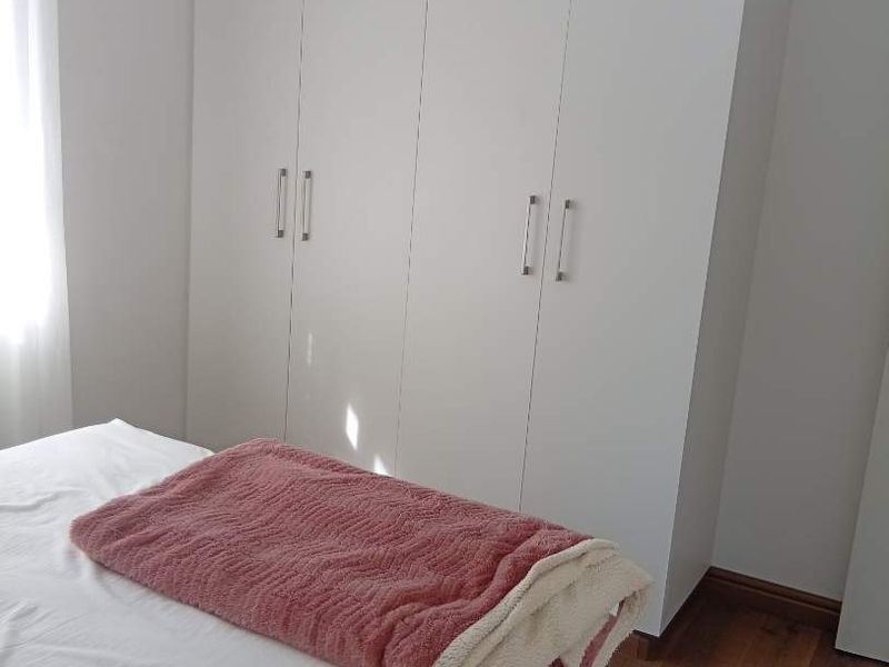 A clean bedroom featuring modern white built-in cupboards and warm-toned laminate flooring, offering a bright and functional living space.