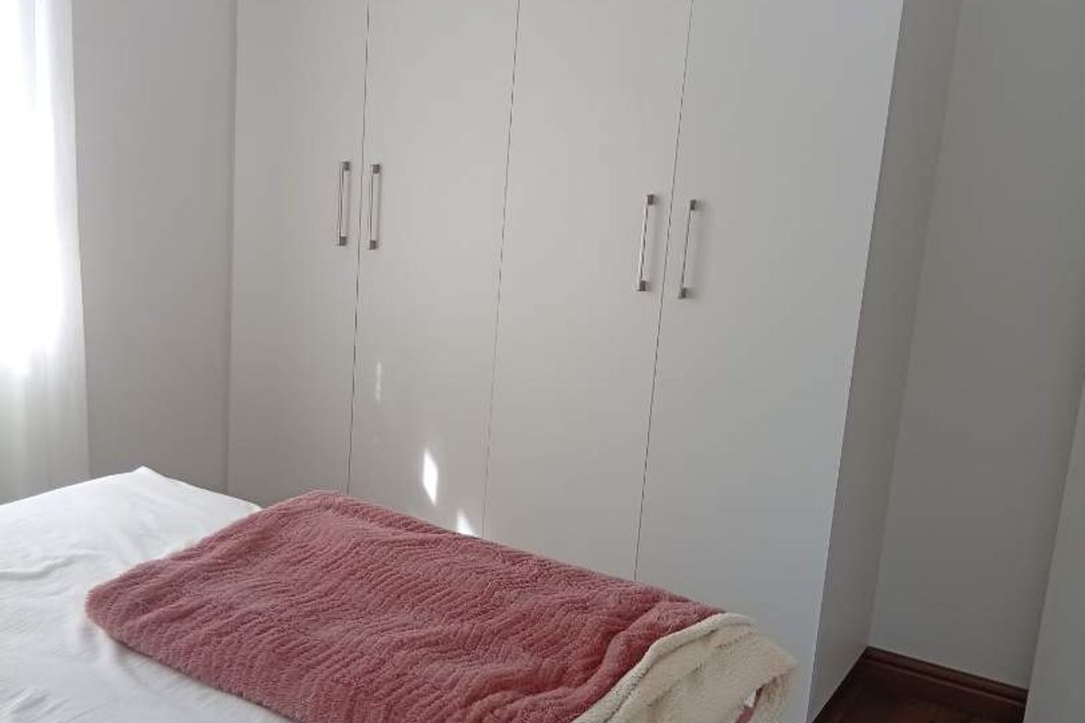 A clean bedroom featuring modern white built-in cupboards and warm-toned laminate flooring, offering a bright and functional living space.