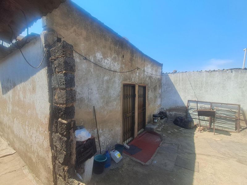 Rear exterior view of a property featuring a weathered concrete structure with security gates and an open yard area.