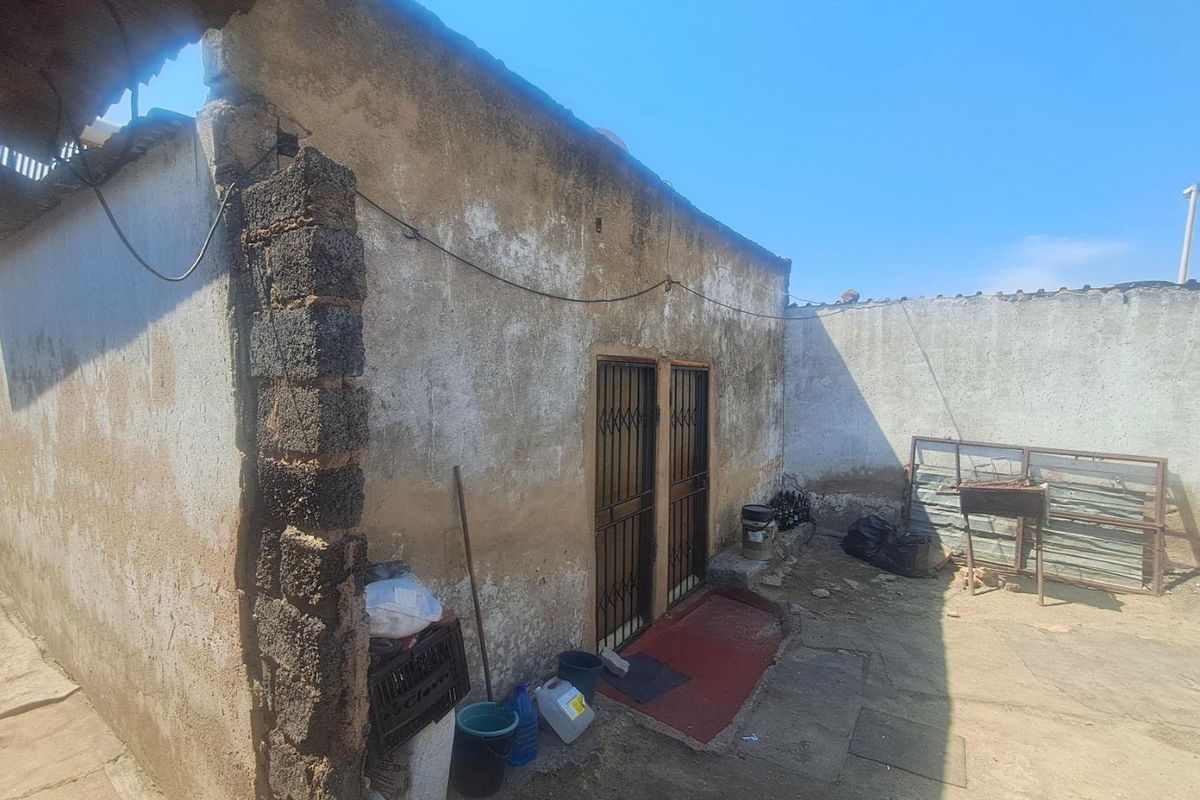 Rear exterior view of a property featuring a weathered concrete structure with security gates and an open yard area.