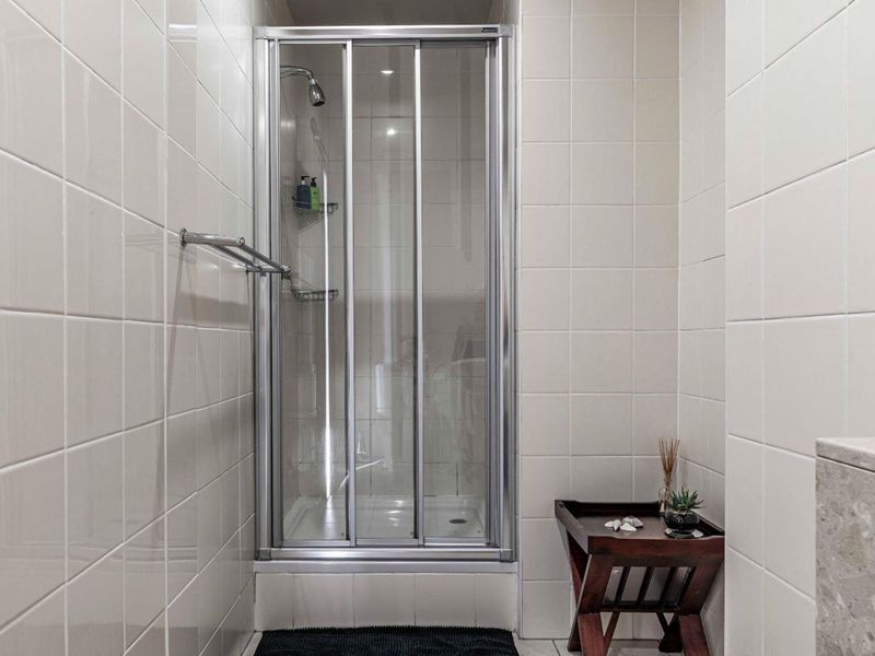A functional bathroom featuring a glass-enclosed shower with tiled walls and a wall-mounted towel rail.