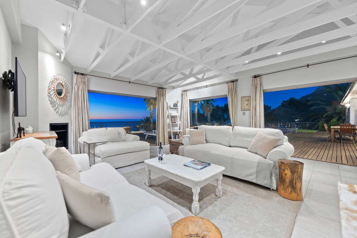 Spacious living room featuring exposed white timber ceiling beams, a built-in fireplace, and large sliding glass doors opening to an outdoor deck with views.