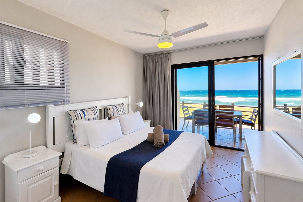 A well-maintained bedroom featuring tiled flooring, a ceiling fan, and sliding glass doors that open onto a balcony with ocean views.