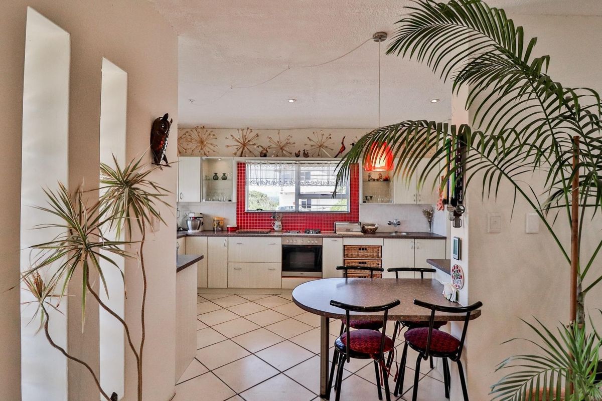 A functional kitchen featuring light-toned cabinetry, a vibrant red tiled backsplash, built-in oven, and tiled flooring, seamlessly connected to a dining area.