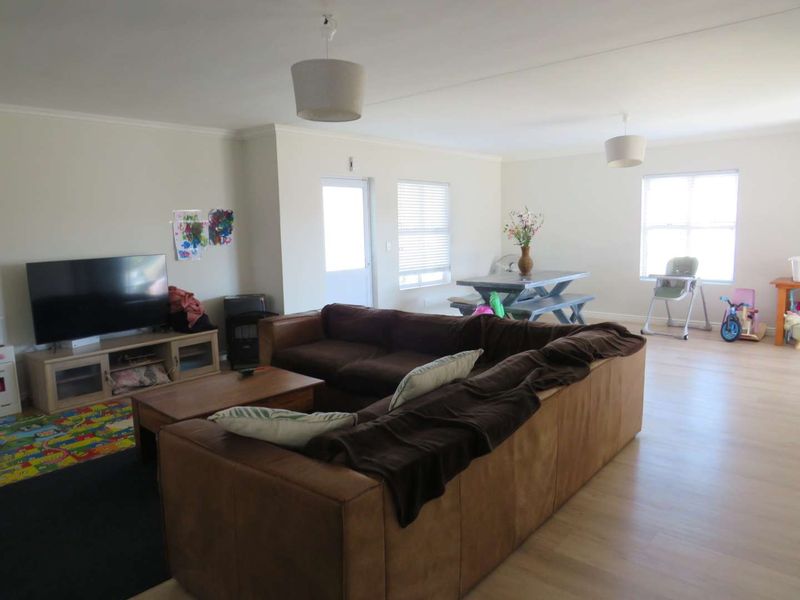 Spacious open-plan living and dining area featuring light-toned laminate flooring, neutral walls, and ample natural light through multiple windows.