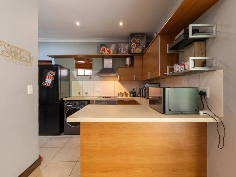 Compact kitchen featuring wood-look cabinetry, stone countertops, built-in oven, extractor fan, and tiled flooring with integrated laundry appliance space.