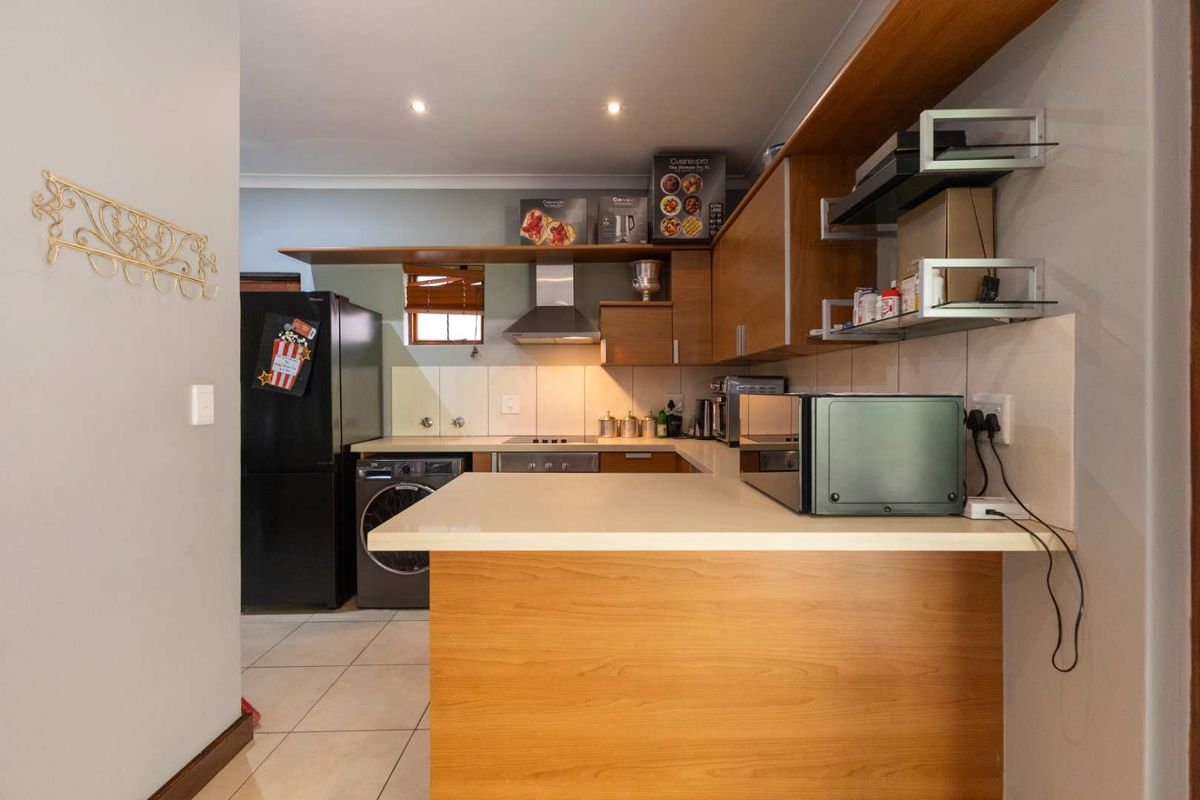 Compact kitchen featuring wood-look cabinetry, stone countertops, built-in oven, extractor fan, and tiled flooring with integrated laundry appliance space.