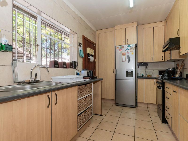 A functional kitchen featuring light wood-finish cabinetry, laminate countertops, a double bowl sink, and tiled flooring with a window providing natural light.