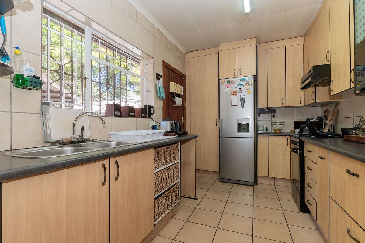 A functional kitchen featuring light wood-finish cabinetry, laminate countertops, a double bowl sink, and tiled flooring with a window providing natural light.