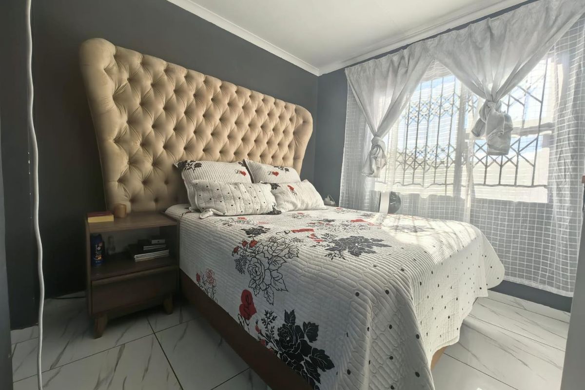 A well-maintained bedroom featuring modern marble-look floor tiles, a dark accent wall, and security bars on the window.