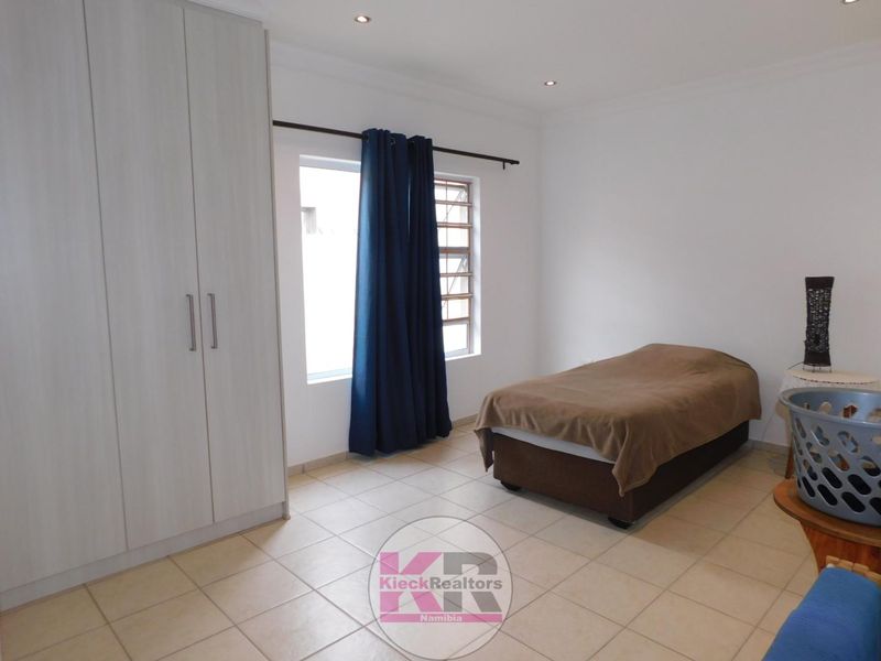 A clean bedroom featuring neutral tiled flooring, built-in wardrobes, and recessed ceiling lighting, offering a functional and well-maintained living space.