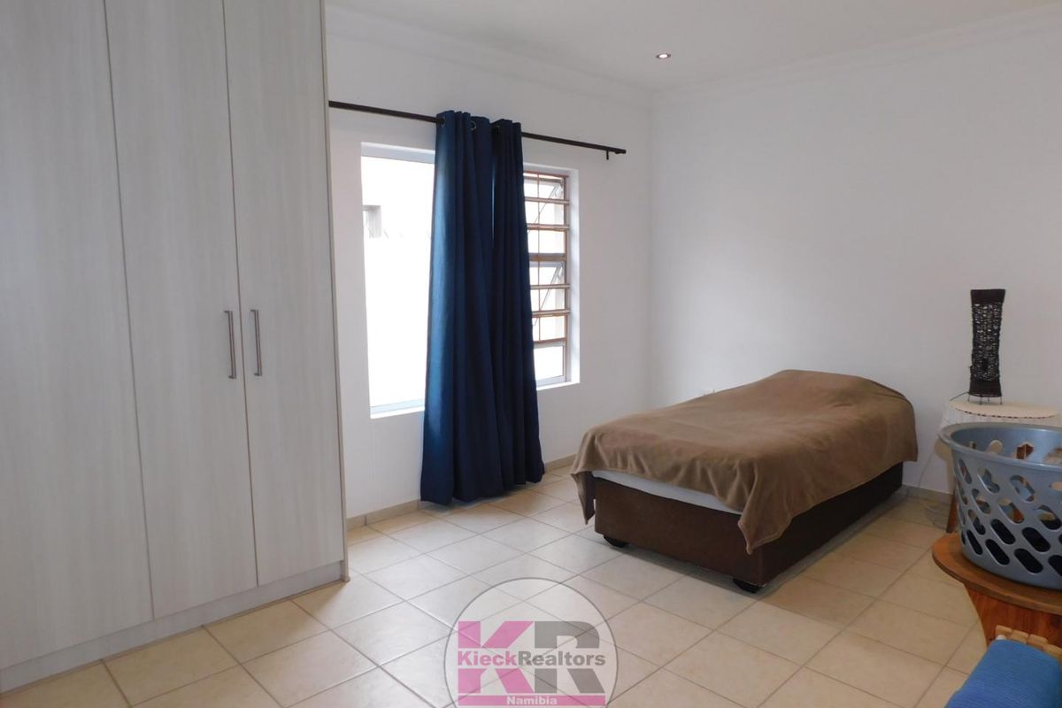 A clean bedroom featuring neutral tiled flooring, built-in wardrobes, and recessed ceiling lighting, offering a functional and well-maintained living space.