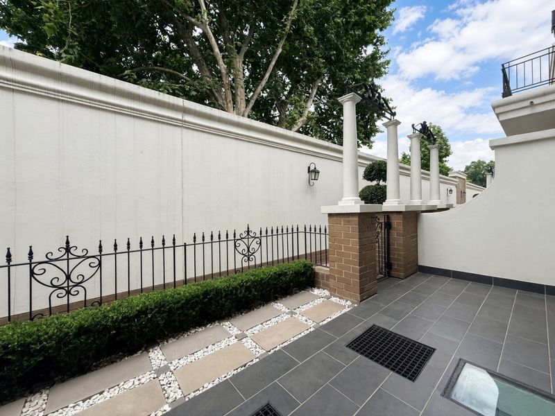 A well-maintained outdoor patio area featuring tiled flooring, decorative brick pillars with columns, and wrought iron fencing, providing a clean and structured exterior space.