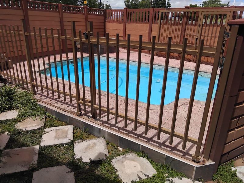 A fenced swimming pool area featuring a paved surround and perimeter boundary wall, providing a secure outdoor space.