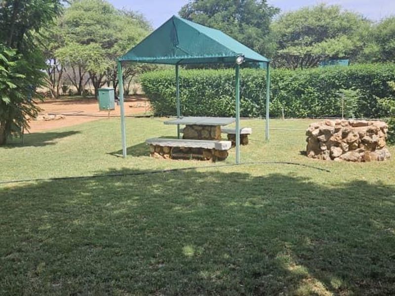 A landscaped garden area featuring a green gazebo, fixed stone seating, a stone fire pit, and mature trees.