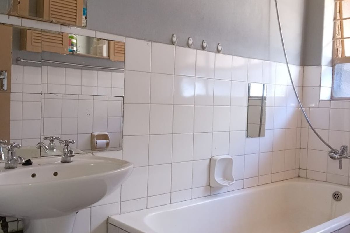 A functional bathroom featuring a pedestal basin, bathtub with shower attachment, and wall-mounted electric water heater with exposed plumbing.