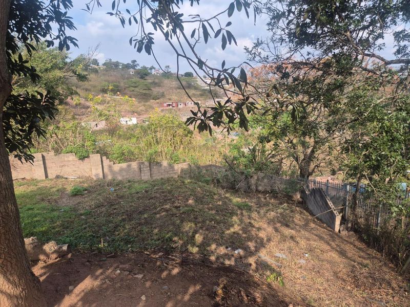An elevated view of the property's rear boundary, featuring concrete block walls, metal fencing, and sloping natural terrain with surrounding trees.