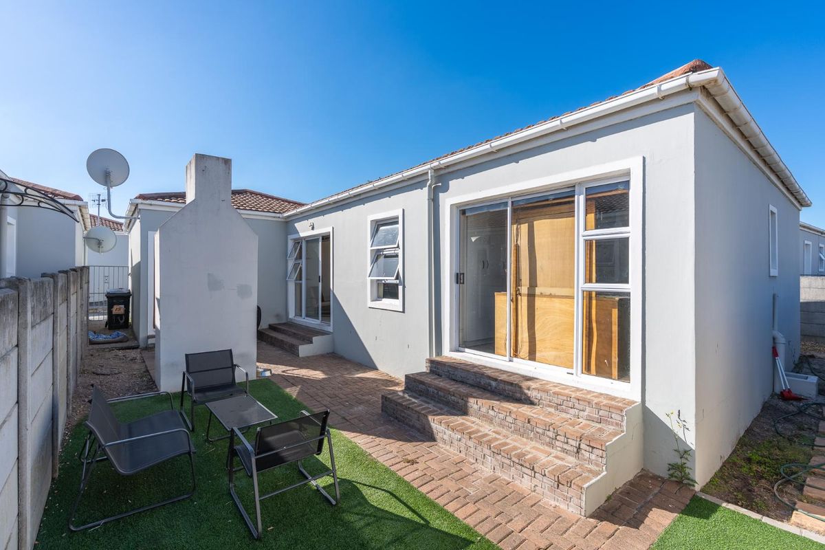 Rear exterior view featuring a paved patio area, built-in braai, and sliding door access to the main living space.