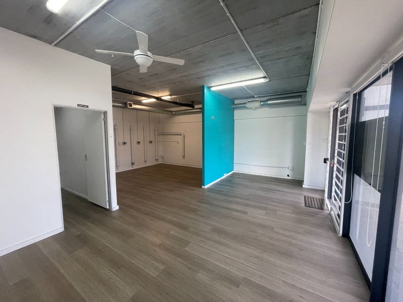 Open-plan retail or office space featuring exposed concrete ceilings, modern laminate flooring, and a bright blue accent wall with functional utility ducting.
